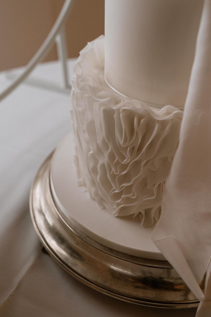 Wedding cake in South Shields. A close-up of a white, ruffled wedding cake on a silver stand, draped with a piece of white fabric.