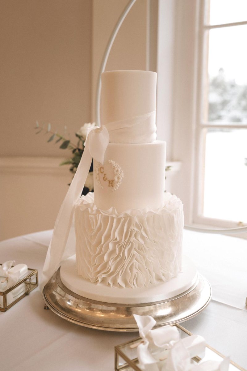 Wedding cake in South Shields. A three-tier white wedding cake with ruffled icing on the bottom tier, a ribbon around the top tier, and an "E & N" monogram is displayed on a silver platter.