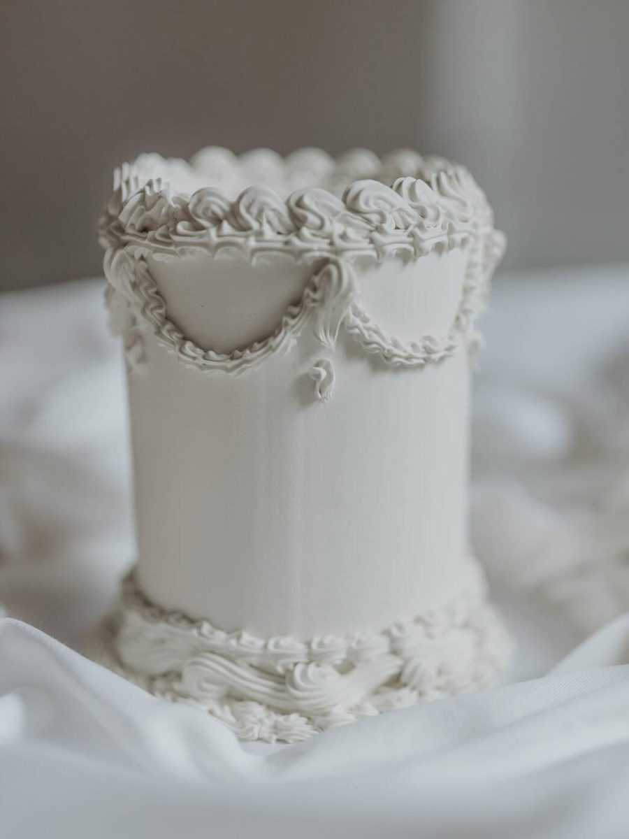 Elegant white cake crafted by a renowned Cake Designer in the North East, featuring intricate icing swirls and scalloped edges, beautifully displayed on a white fabric background.