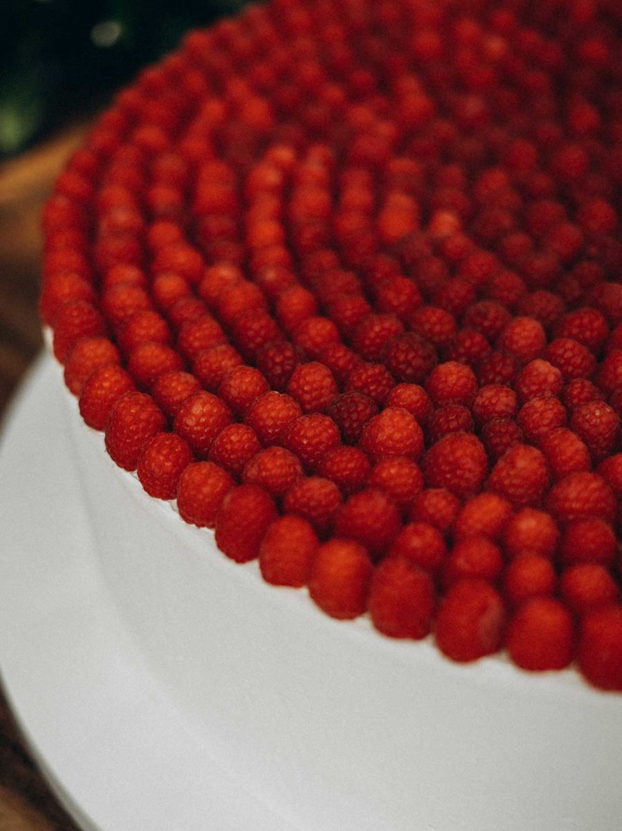 A round cake covered with a smooth white frosting and topped with concentric rows of fresh raspberries.